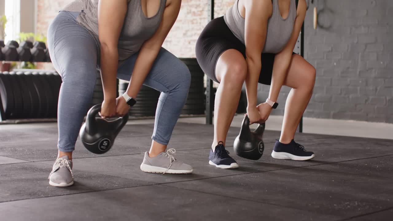 Istruttore di fitness che mostra il kettlebell swing in palestra, cliente che ne imita la forma per acquisire potenza