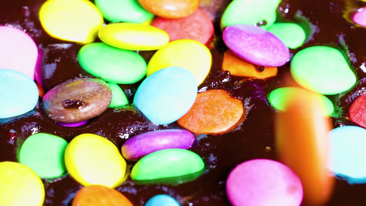 A close-up view of colorful candies scattered over a rich, dark chocolate surface.