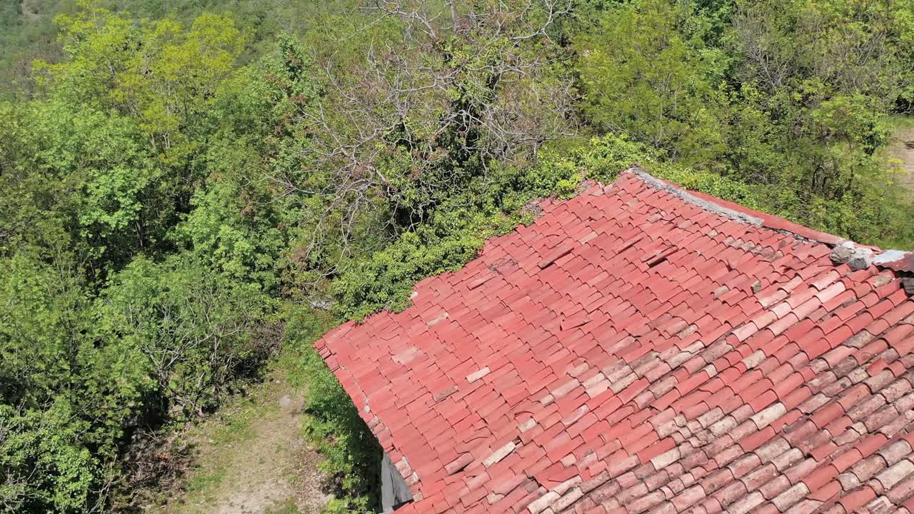 Deep flight over a Mediterranean old farmhouse with red roofs surrounded by forests. Drone shot
