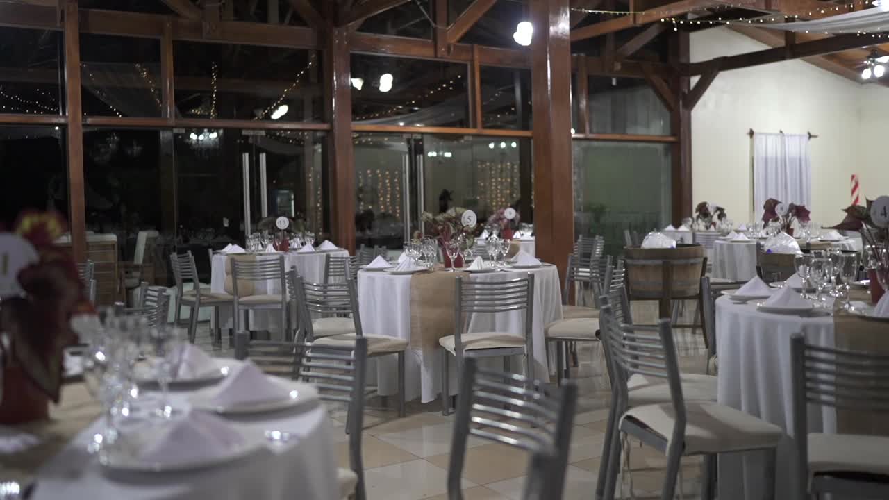 Clean, left pan reveals elegant wedding decor with white tables, silver chairs, and a large wooden windows