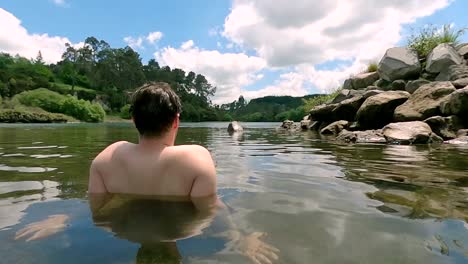 peacful scene of man sitting in thermal spring looking out into the wilderness downstream