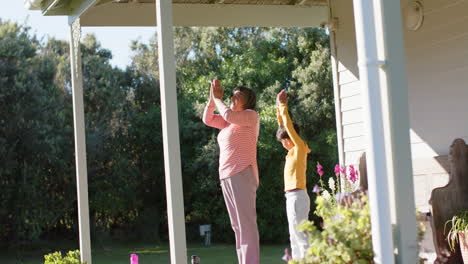 Senior-biracial-grandmother-and-grandson-doing-yoga-and-meditating-on-terrace-at-home,-slow-motion