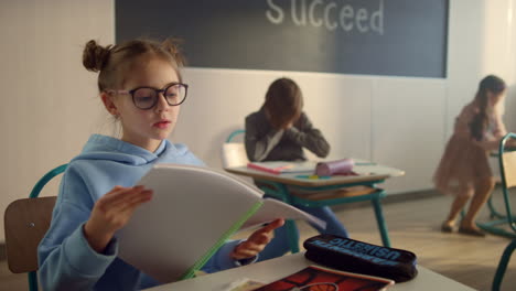 cute girl sitting at desk at school. clever pupil opening notebook in classroom