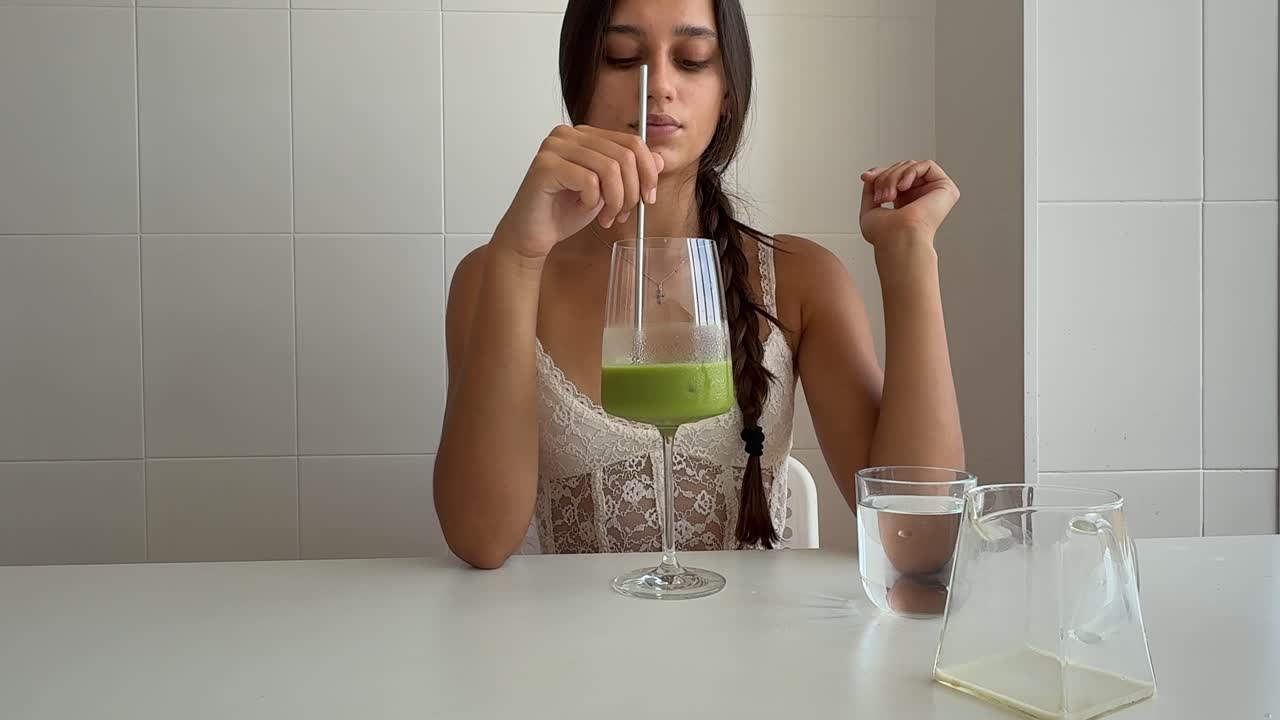 Giovane donna beve un frullato verde a casa