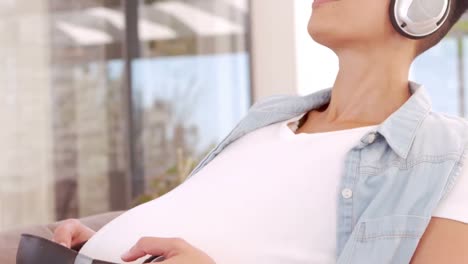 happy pregnant woman listening to musing and putting headphones on her belly