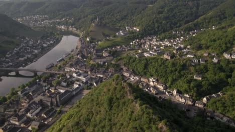 Toma-Aérea-Giratoria-Alrededor-De-Un-Pico-De-Montaña,-Con-Cochem,-El-Castillo-De-Cochem-Y-El-Río-Moselle-En-El-Fondo