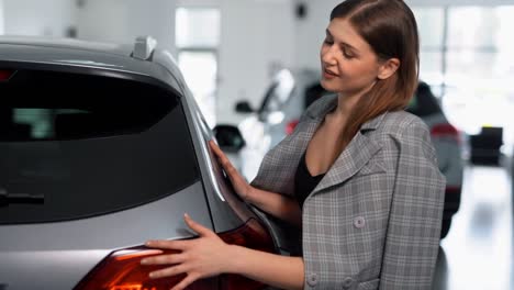 mujer elegante con traje de negocios abraza un auto en un concesionario de autos