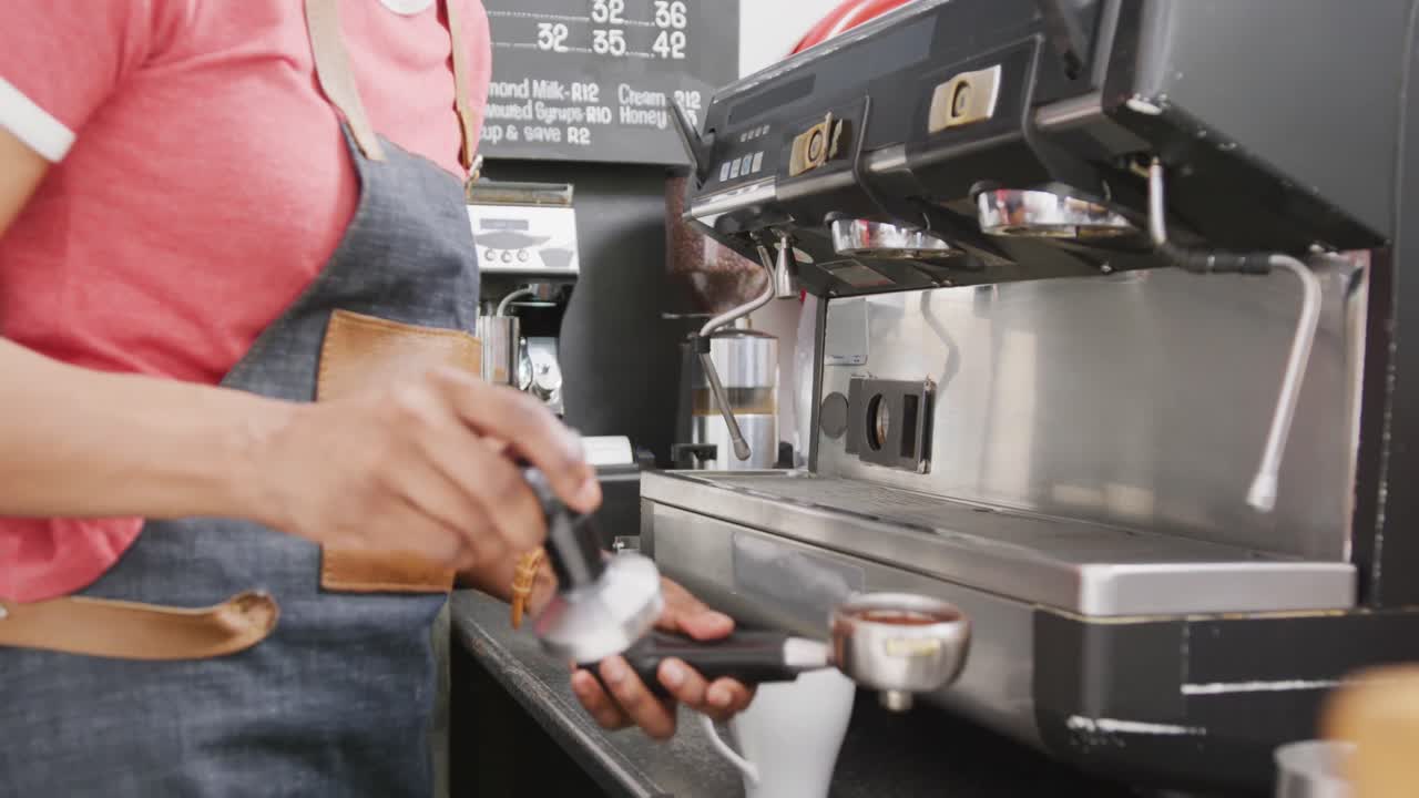 Barista donna di etnia mista con grembiule che prepara il caffè con la macchina del caffè in caffetteria.