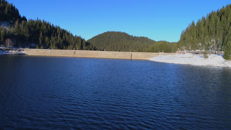 aerial: flying above the water of a dam blocked by a dam wall in winter