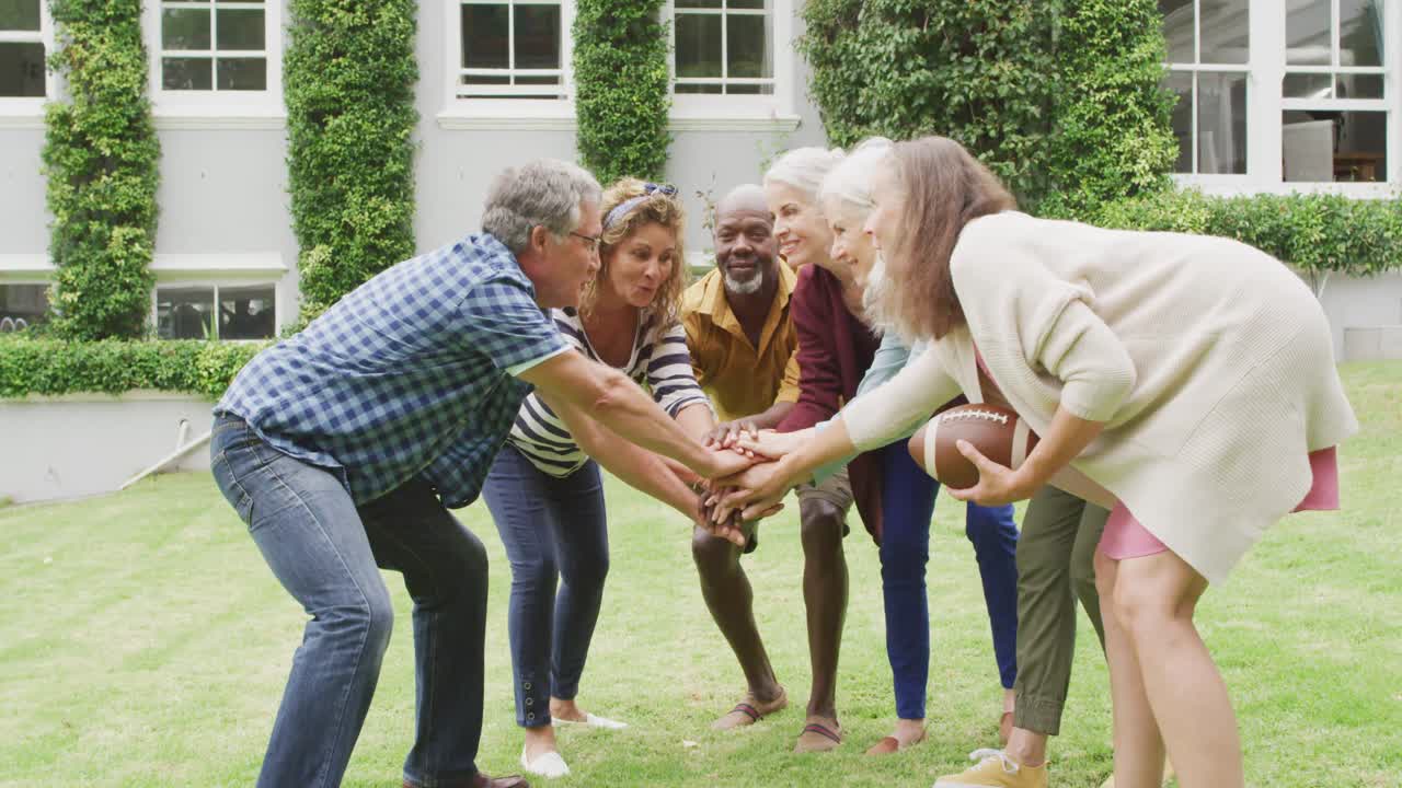 animación de felices y diversas mujeres y hombres amigos mayores jugando al fútbol americano en el jardín