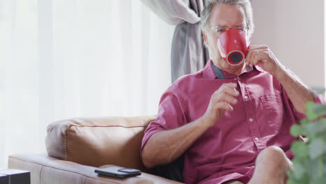 Portrait-of-senior-caucasian-sitting-on-sofa-and-drinking-coffee,-slow-motion