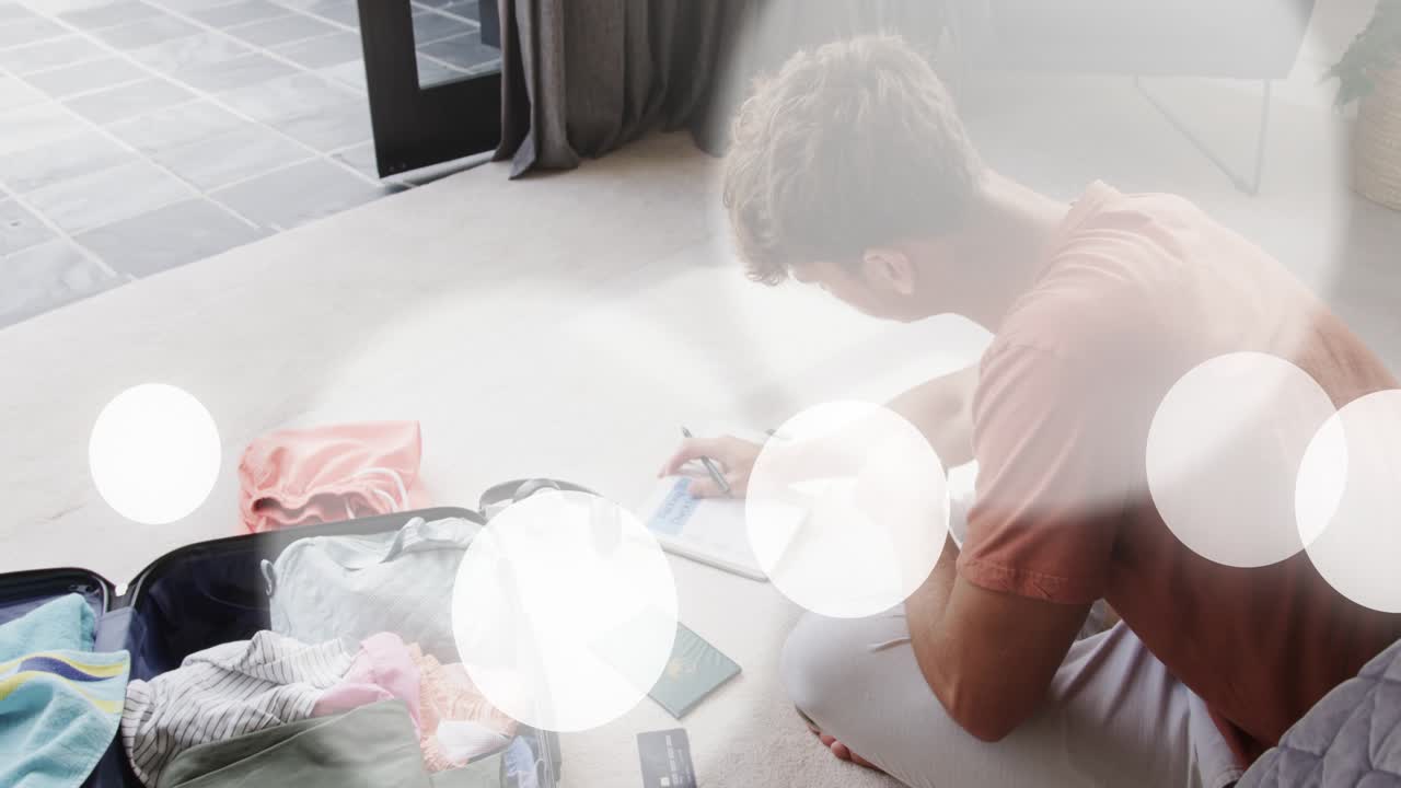 Man tapping tablet and picking up passport and card, preparing suitcase for trip, noting plan