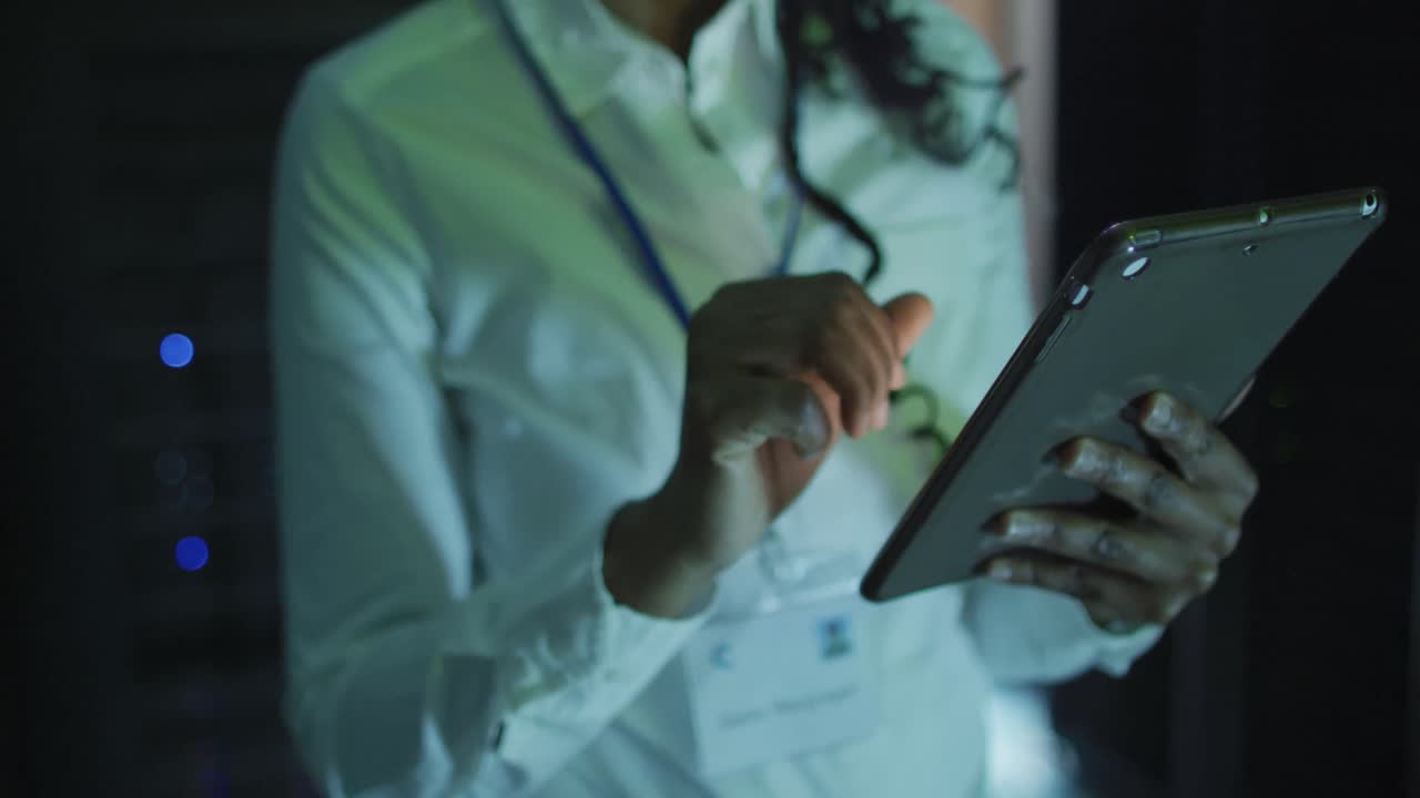 técnica informática afroamericana que usa una tableta trabajando en una sala de servidores de negocios