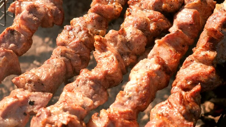 Appetizing juicy pork barbecue is roasted on skewers on top of charcoal grill. Close-up meat pieces.