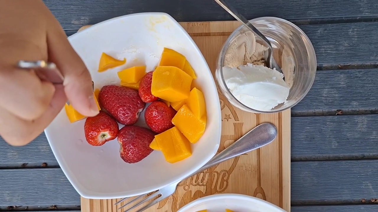 Vista dall'alto di un bambino che raccoglie un pezzo di mango con la forchetta da una ciotola di frutta all'aperto