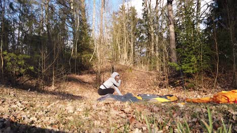 female camper building up a tent alone in the forest - wide shot, static