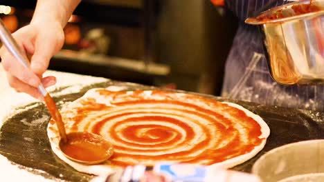 chef spreads sauce on pizza dough