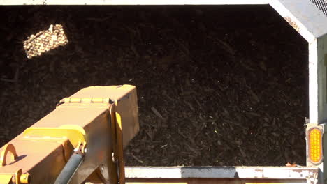 slow-motion shot of wood chips expelled from the chute of a wood chipper into the back of a truck