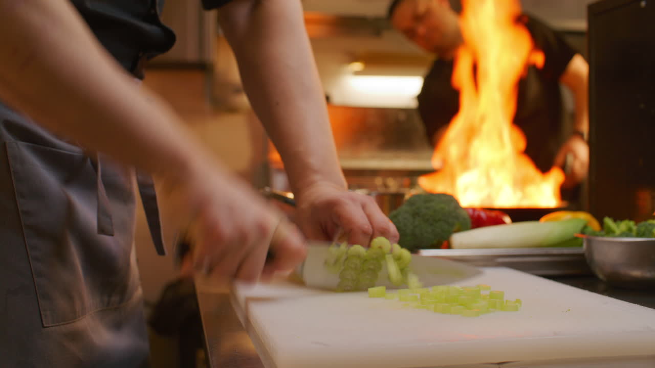 Restaurangkock hackar selleri medan en kollega flamberar mat i köket