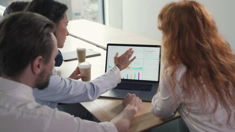 un joven equipo de trabajo compuesto por dos mujeres y dos hombres consultando resultados financieros en la computadora portátil en una reunión de trabajo