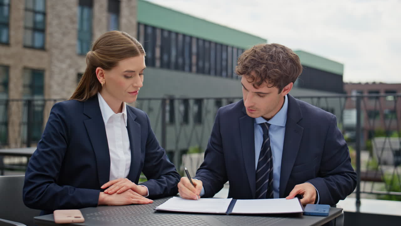Focused partners reviewing paperwork at meeting at rooftop workspace closeup