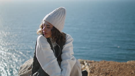 Serene-girl-enjoy-music-on-ocean-cliff-vertical.-Dreamy-woman-with-closed-eyes