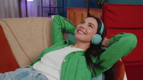mujer joven feliz con auriculares inalámbricos relajándose acostada en el sofá en casa escuchando su música favorita