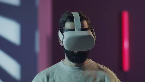 a bearded man wearing a vr headset looks around, fully immersed in a virtual experience. the futuristic room with neon lights enhances the theme of the metaverse and modern technology.