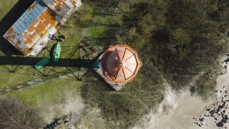 Aerial-establishing-view-of-white-colored-Pape-lighthouse,-Baltic-sea-coastline,-Latvia,-white-sand-beach,-large-waves-crashing,-sunny-day-with-clouds,-ascending-drone-birdseye-shot