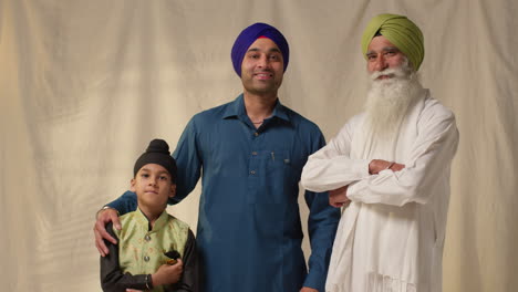 studio portrait shot of multi generation male sikh family wearing turbans standing against plain background