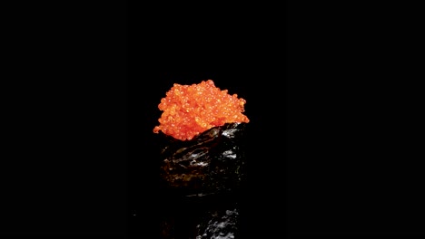 shrimp roe sushi rotates smoothly under dramatic lighting, isolated against a seamless black background, highlighting vibrant orange roe and glossy seaweed wrap