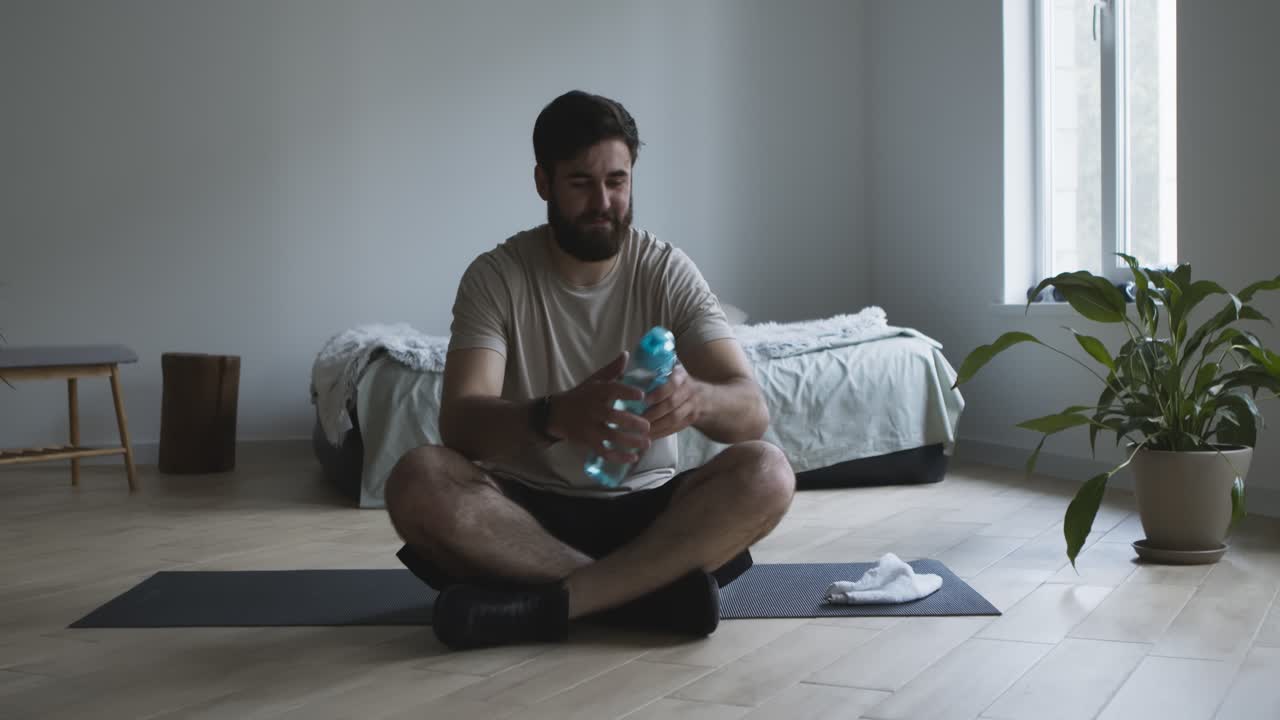 hombre tomando un descanso del ejercicio y bebiendo agua en casa