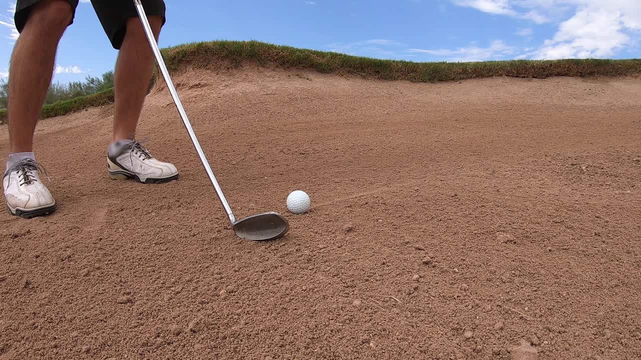 골퍼가 골프공 뒤에 샌드 아이언을 정렬한 다음 애리조나주 스코츠데일의 샌드트랩에서 공을 칩니다.