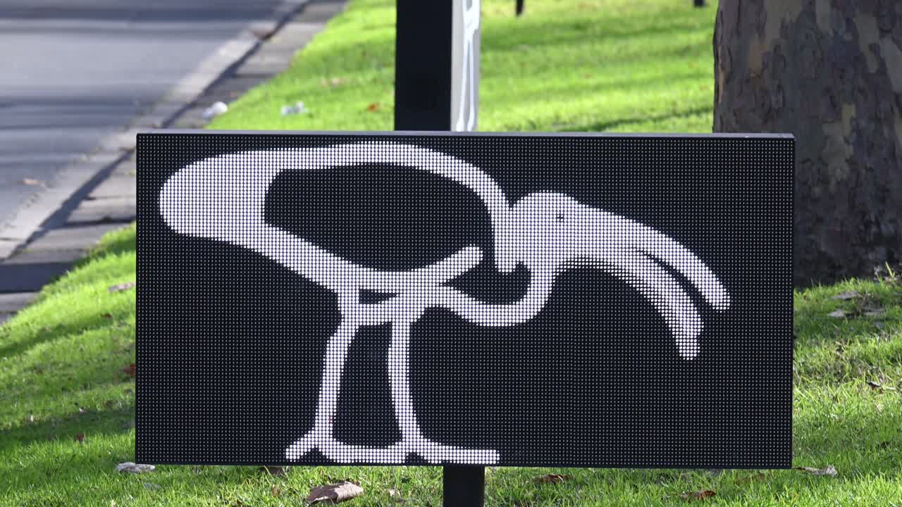Electronic road sign shows stylised ibis bird symbol beside green verge