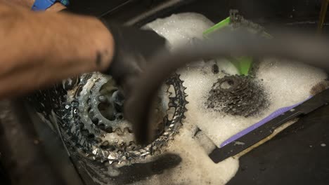 male bicycle mechanic scrubs a chainring in a workshop basin