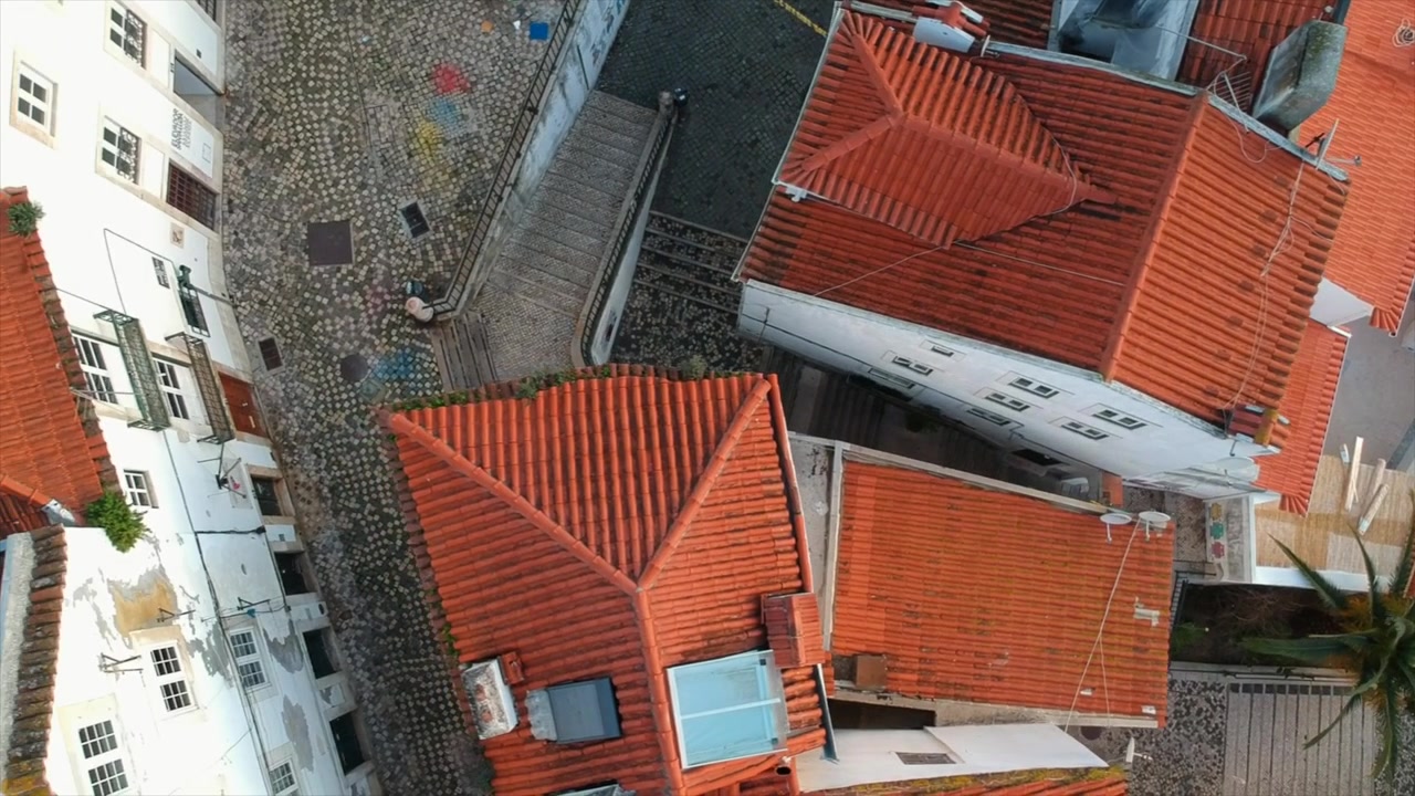 Panoramica aerea dall'alto sui tetti in terracotta iconici di Lisbona e sull'architettura storica, strade e cortili piastrellati.