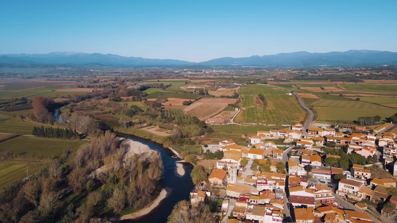 Una splendida vista aerea di un bellissimo villaggio immerso tra i campi coltivati con un fiume su un lato, che avanza con montagne distanti sullo sfondo