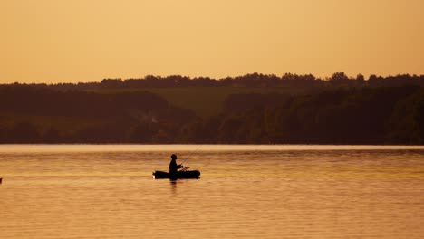 silhouette of a man with fishing rods in the middle of the lake at sunset. natural river background in the evening and a fisherman in a boat.