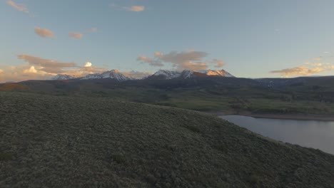 Beautiful-sunset-slow-panning-back-establishing-shot-over-mountain-hillside-in-snow-covered-rocky-mountains-and-lake