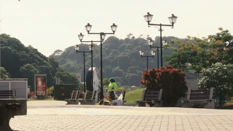 a female public worker of the sanitations authority of panama city, preoccupied while tying a knot in a plastic bag of the trash bin she has just emptied in a park, causeway of amador, panama city