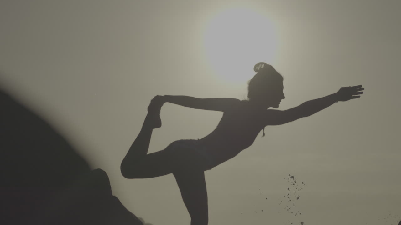 Woman practicing yoga outdoors at sunrise/sunset