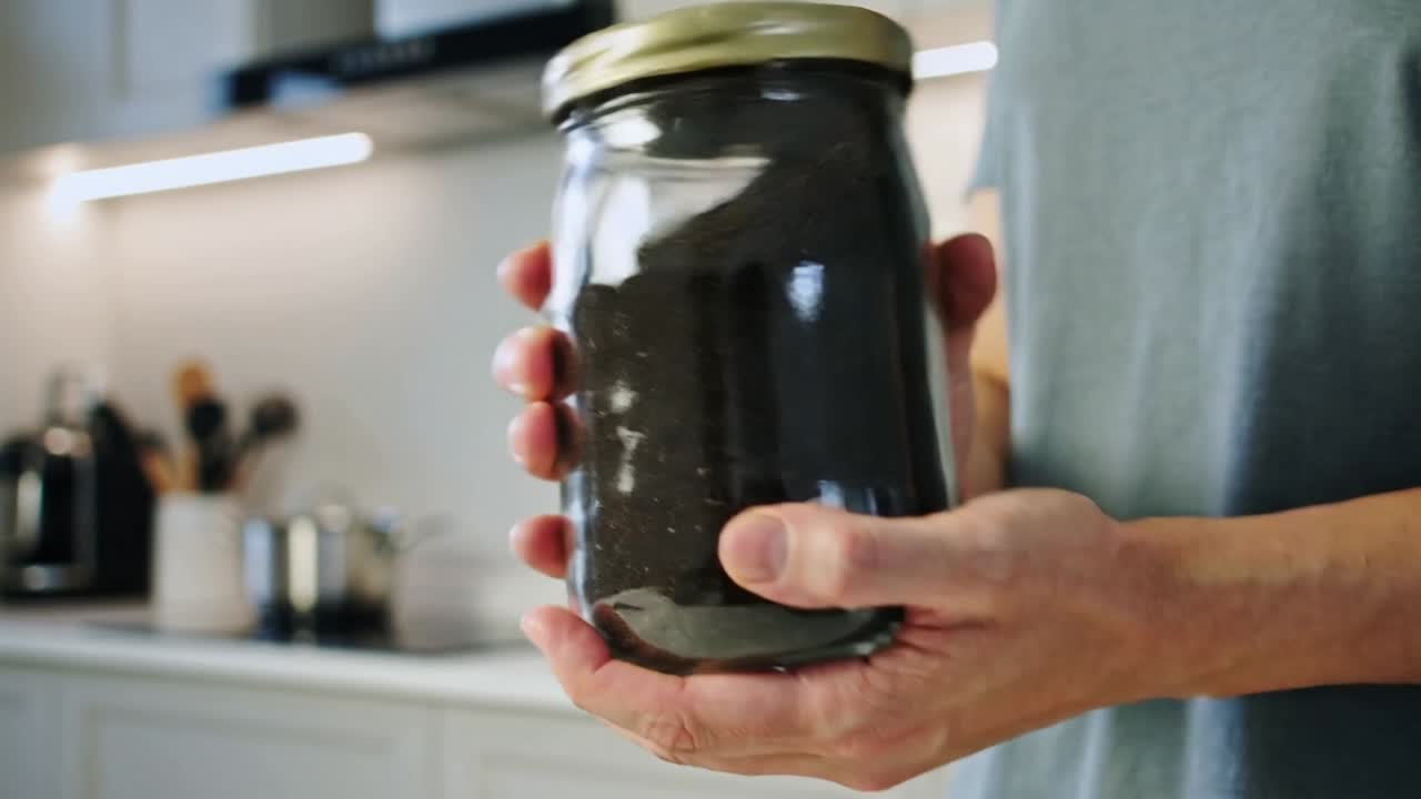 Um adulto segurando uma jarra giratória na cozinha, a mão fazendo o conteúdo se mover e o vidro refletir enquanto inspeciona.