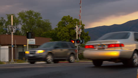 at a railway crossing.  lights are flashing as a train has just passed and the gate rises to allow others through.  cars drive through.