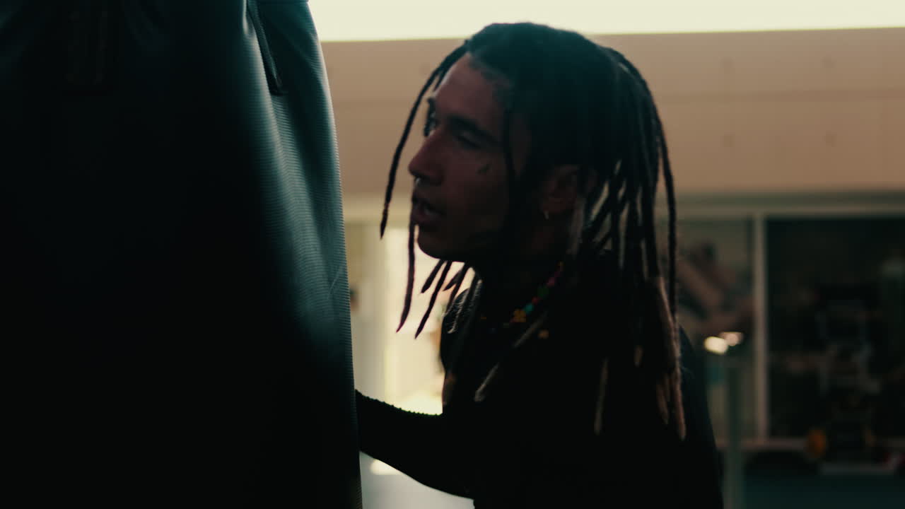 Uomo stanco con i dreadlock che si riposa su un sacco da pugilato in palestra.