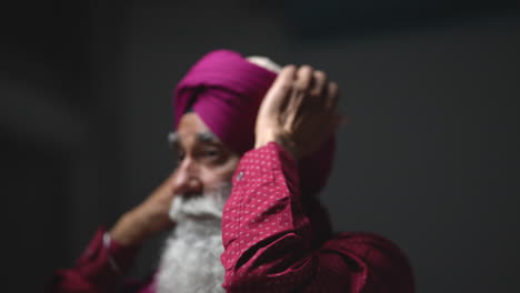 Primer-Plano,-Toma-De-Estudio-Con-Iluminación-Tenue-De-Un-Hombre-Sikh-Mayor-Con-Barba-Atando-Una-Tela-Para-Un-Turbante-Contra-Un-Fondo-Oscuro,-Filmado-En-Tiempo-Real