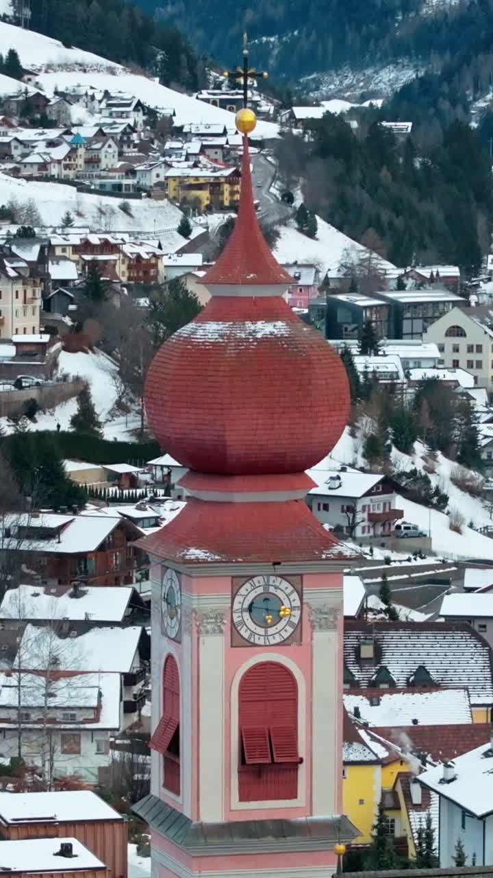 Aerial drone view of the curch in the Ortisei town covered in snow, within the Dolomites, in northern Italy. Vertical