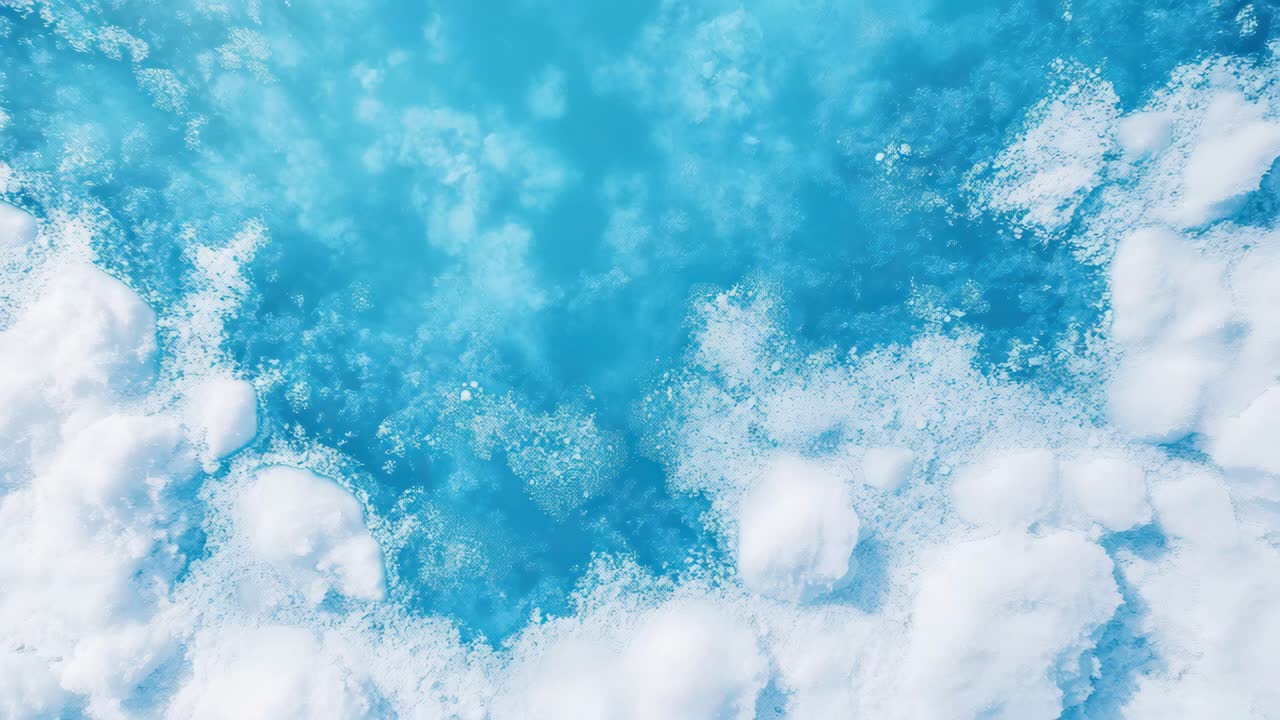 Aerial view of icy blue water with snow patches, creating a serene, abstract pattern