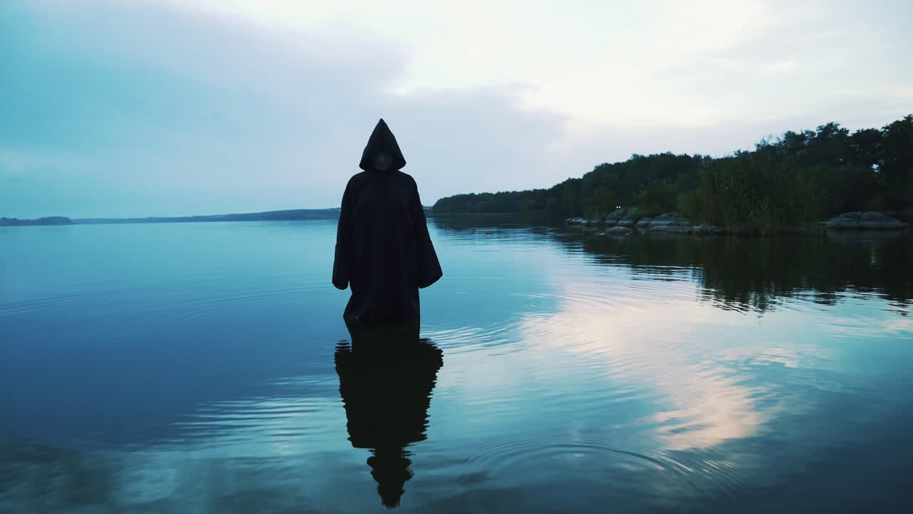 Scary figure in black mantle in the river. Halloween costume.