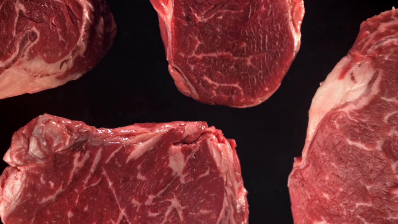 Raw Beef Steaks Falling in Slow Motion on Black Background