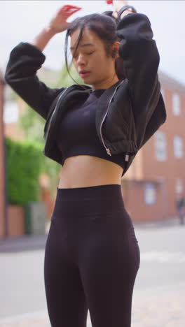 Vertical-Video-Of-Young-Woman-Exercising-Running-On-Urban-Street-Wearing-Wireless-Earbuds-Checking-Smart-Watch